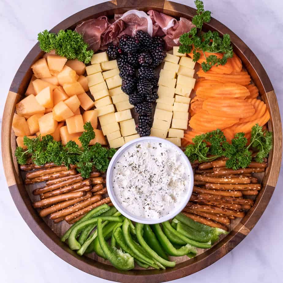 Easter charcuterie board with fruits, meats, cheeses, vegetables, dip, and pretzels.