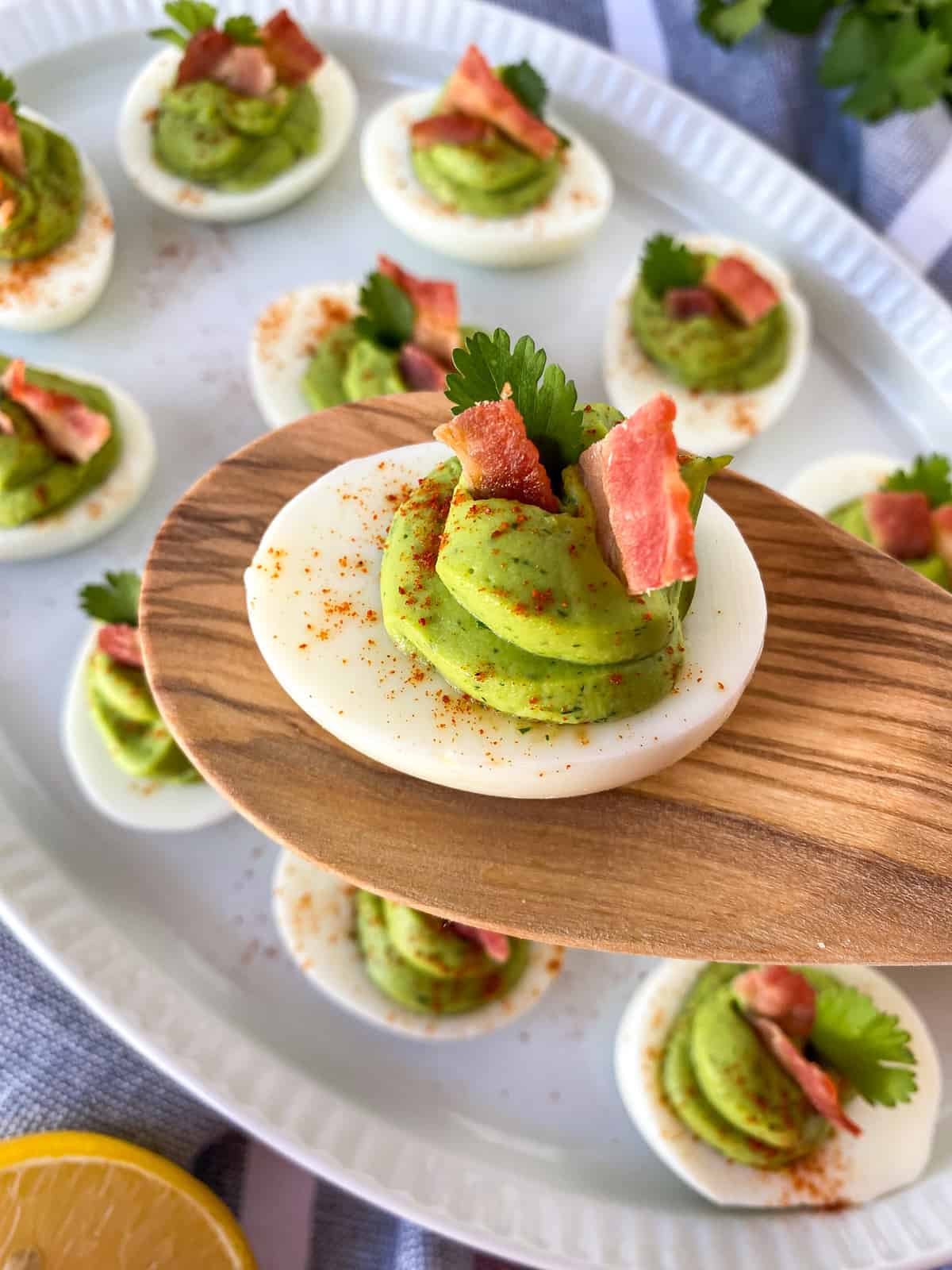 Bacon avocado deviled eggs with no mayo. They are on a white platter with bacon on top of avocado mixture