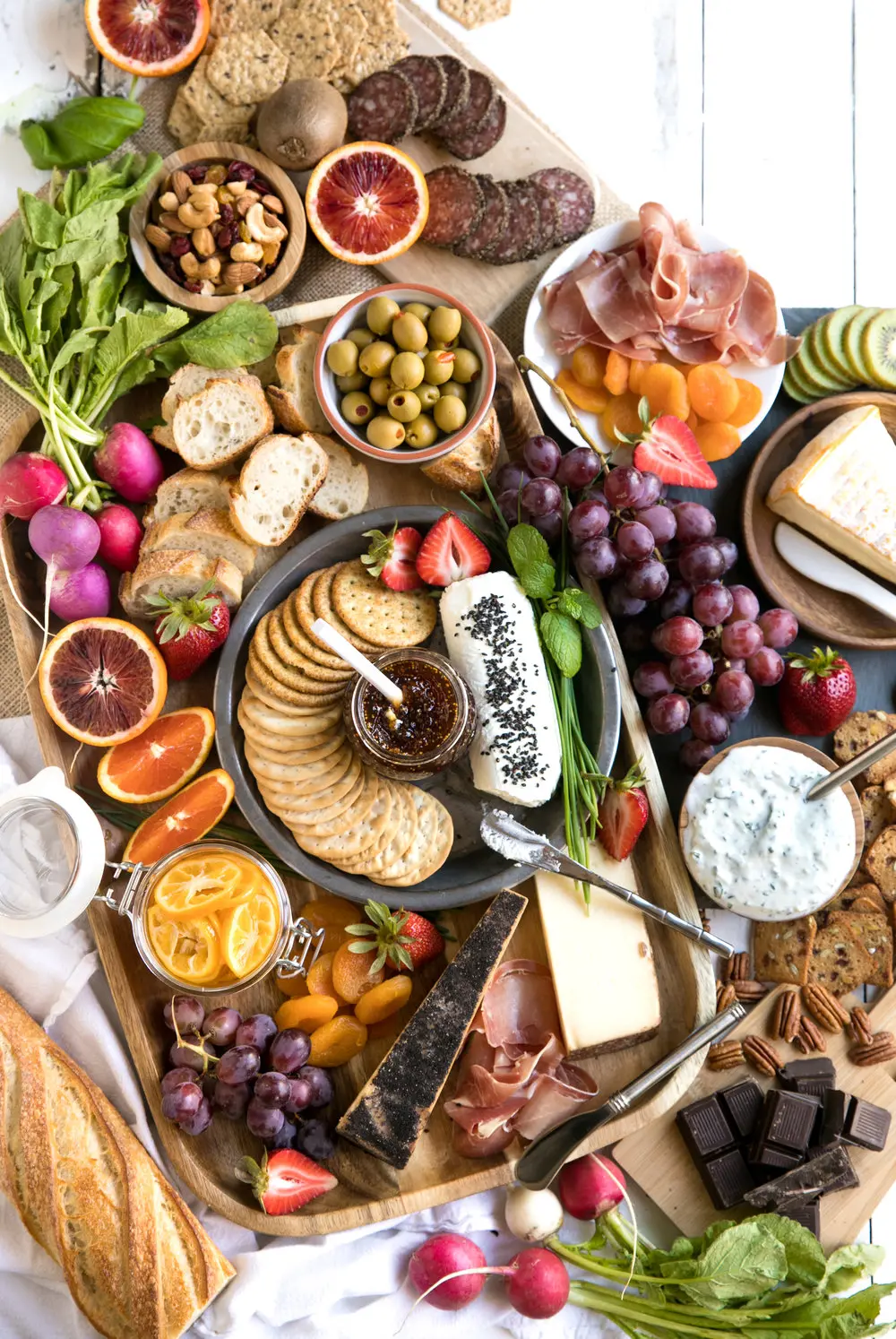 Colorful spring charcuterie board with crackers, fruits, cheeses, olives, and meats.