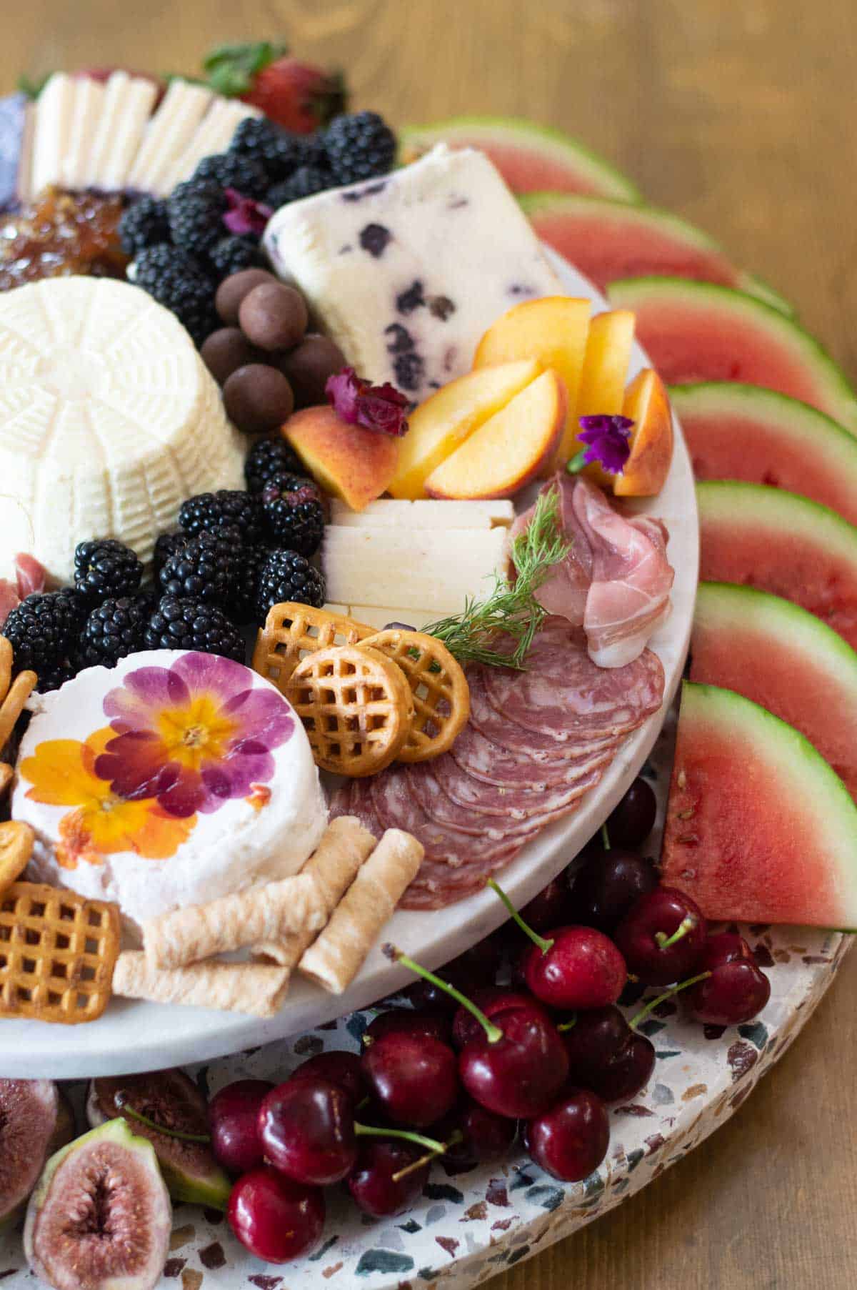 Summer charcuterie board with watermelon, berries, apples, meats, pretzels, and cheeses.
