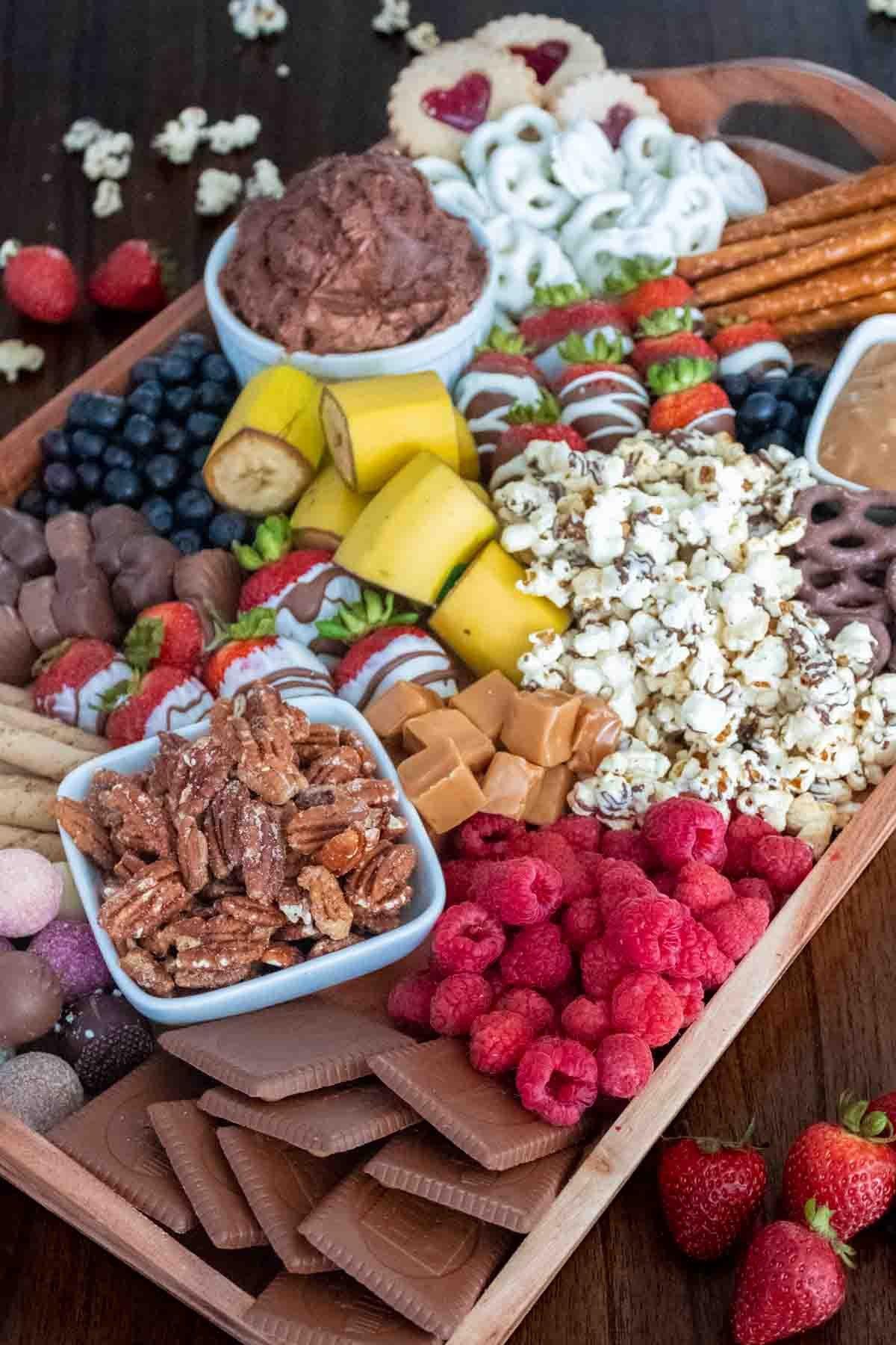 Dessert charcuterie board with chocolate covered pretzels, strawberries, popcorn, bananas, chocolates, and blueberries.