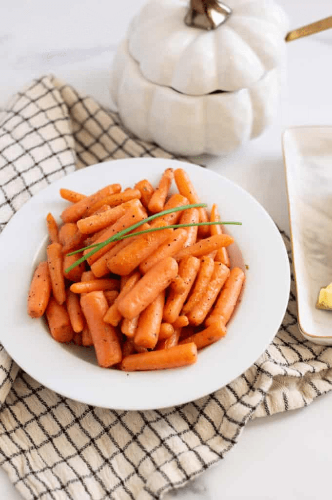 Instant pot carrots in a white bowl with a checkered towel near it