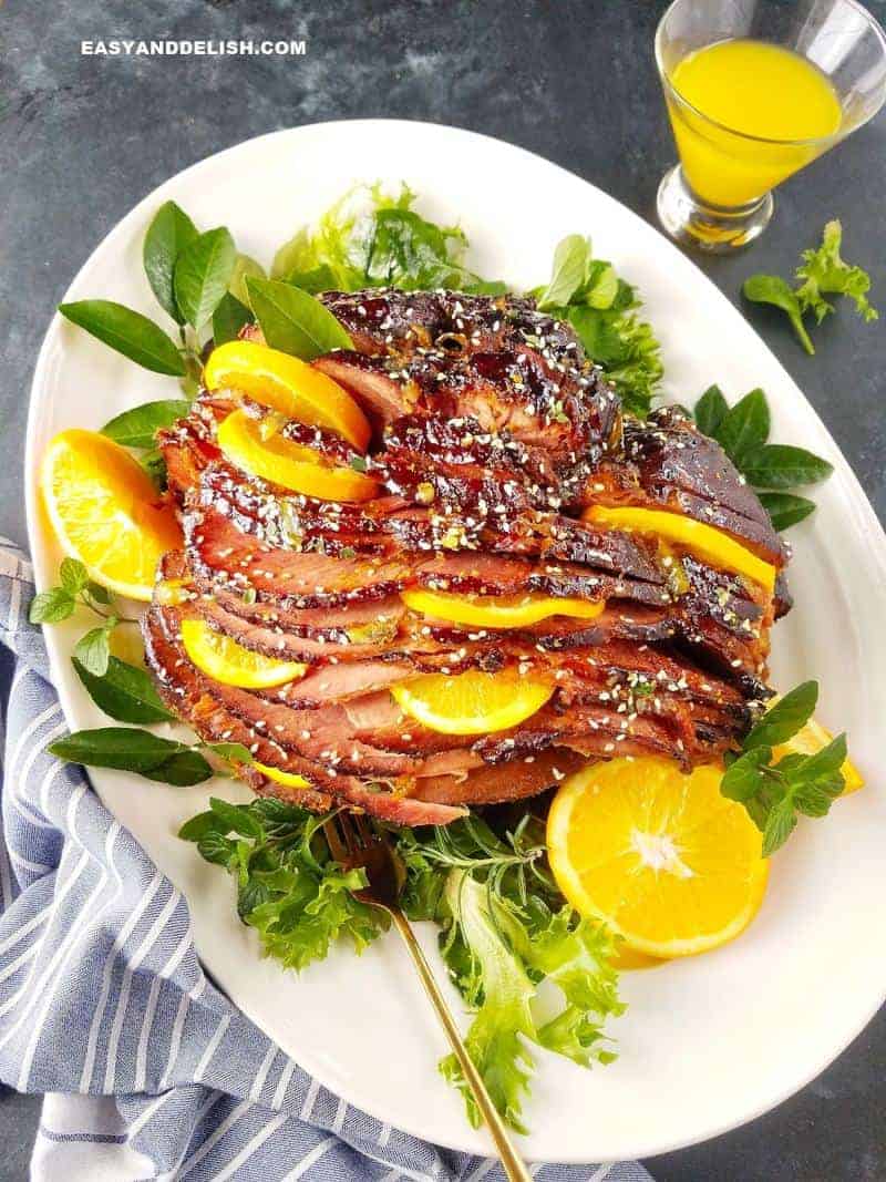 Slow Cooker Ham Recipe with Orange Glaze. Ham cut up with orange slices in between slices. Garnished with lettuce on a white plate.