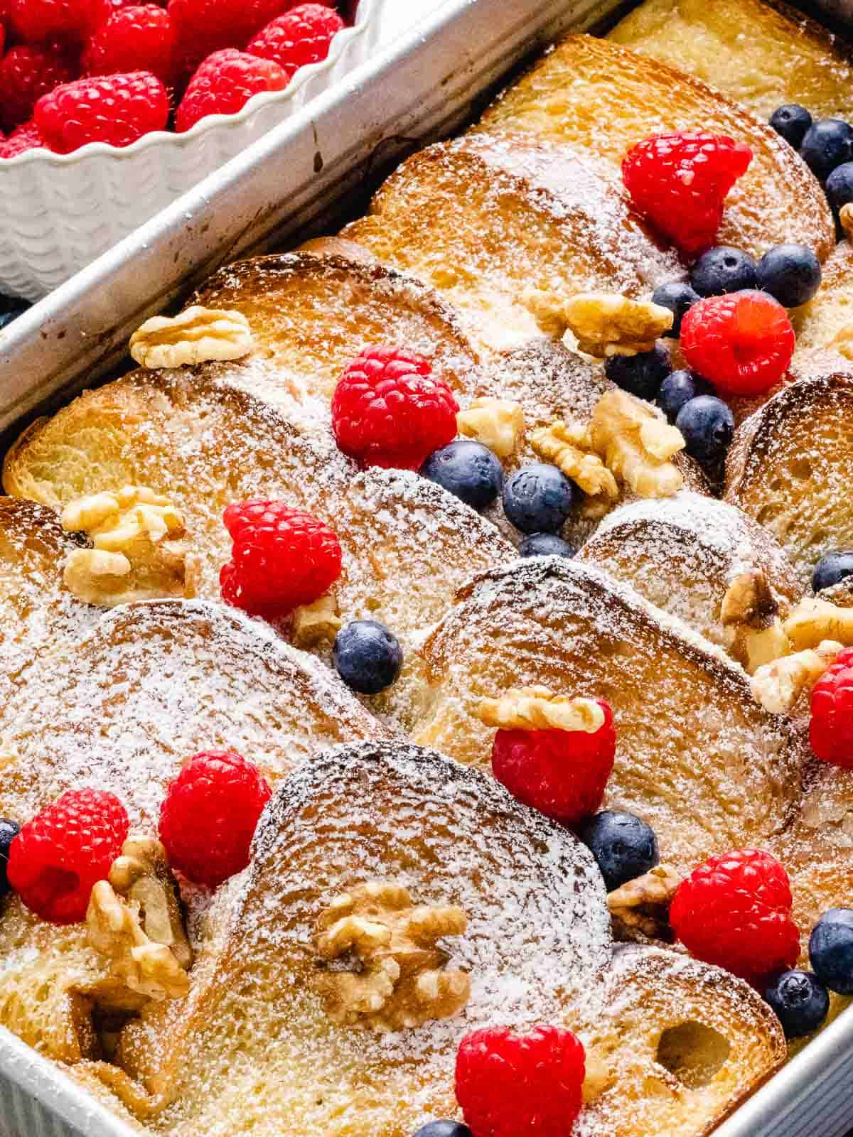 Baked French toast casserole with raspberries, blueberries, powdered sugar, and walnuts on top