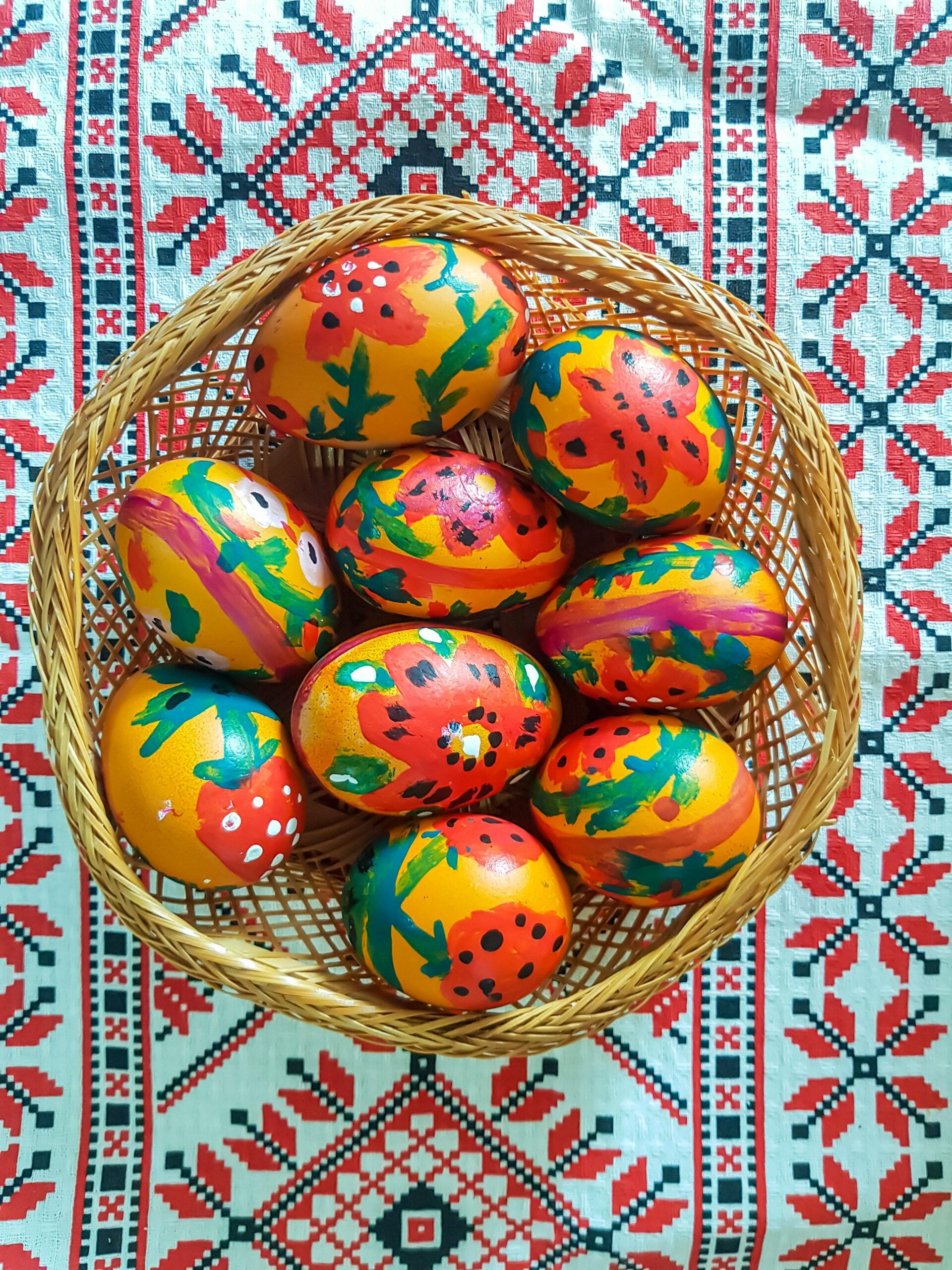 Hand-painted Easter eggs with a yellow base and red, pink, and green artwork. Some have strawberries and some have flowers.