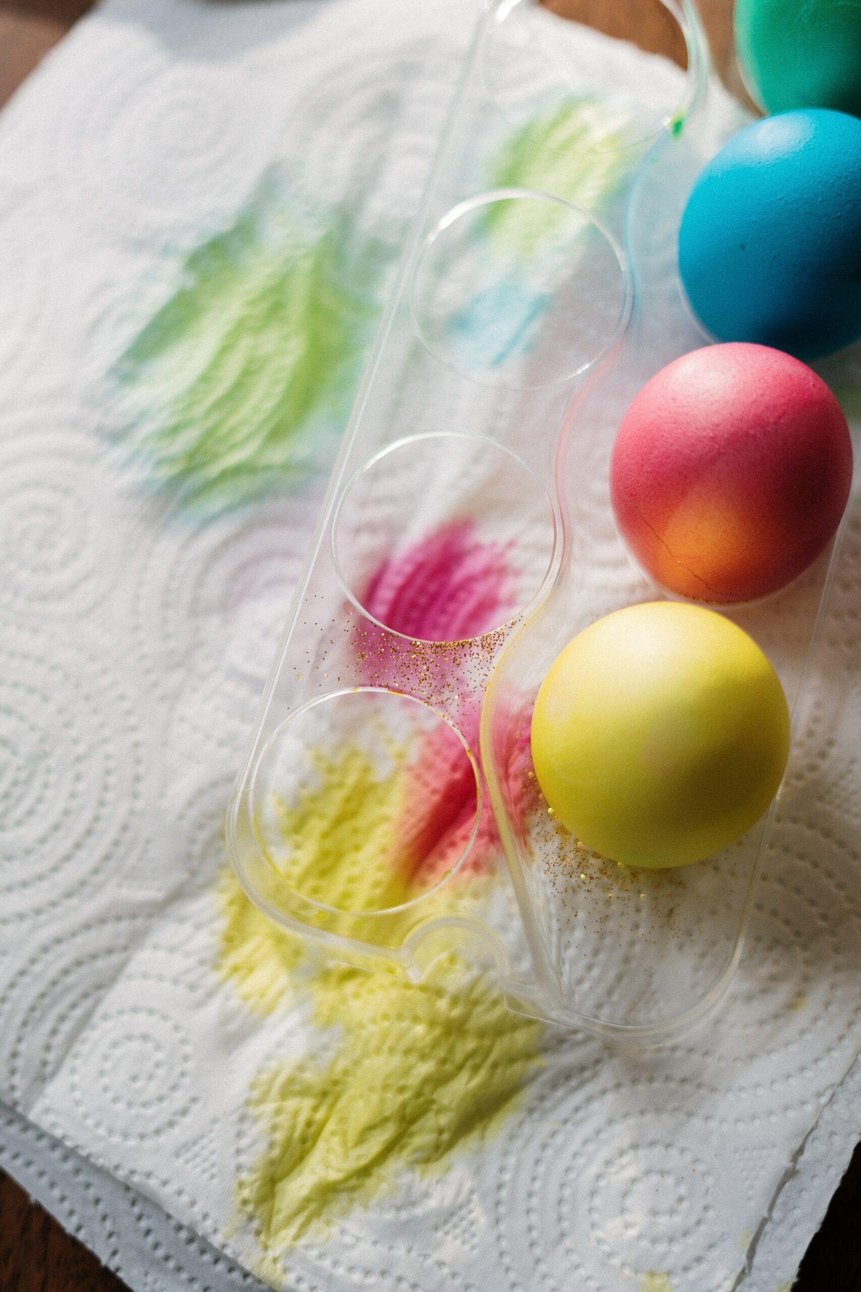 Yellow, blue, pink, and green color dyed Easter eggs right after being dyed. They are drying in a clear plastic egg holder.
