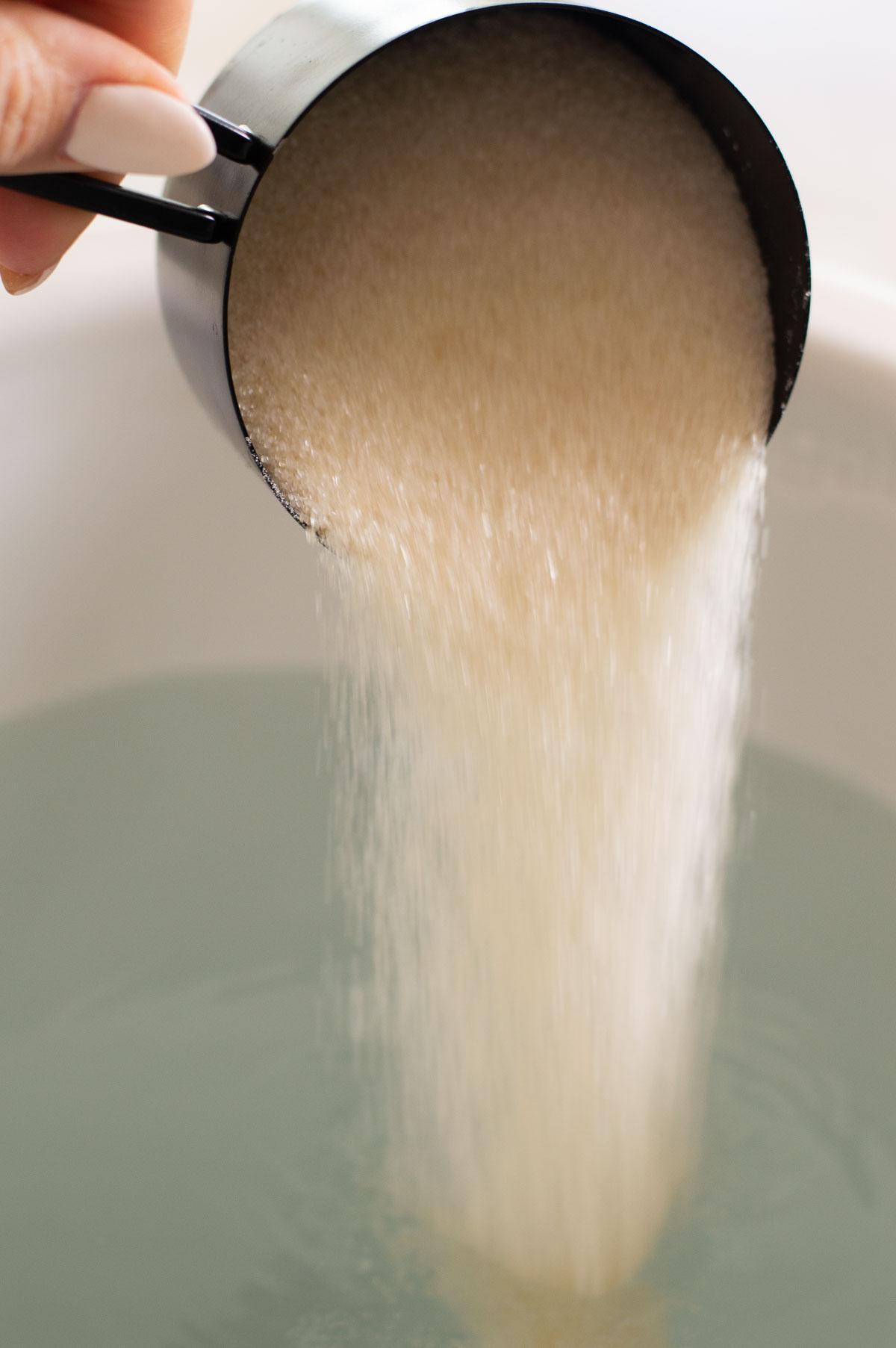 sugar being poured into a bowl of water