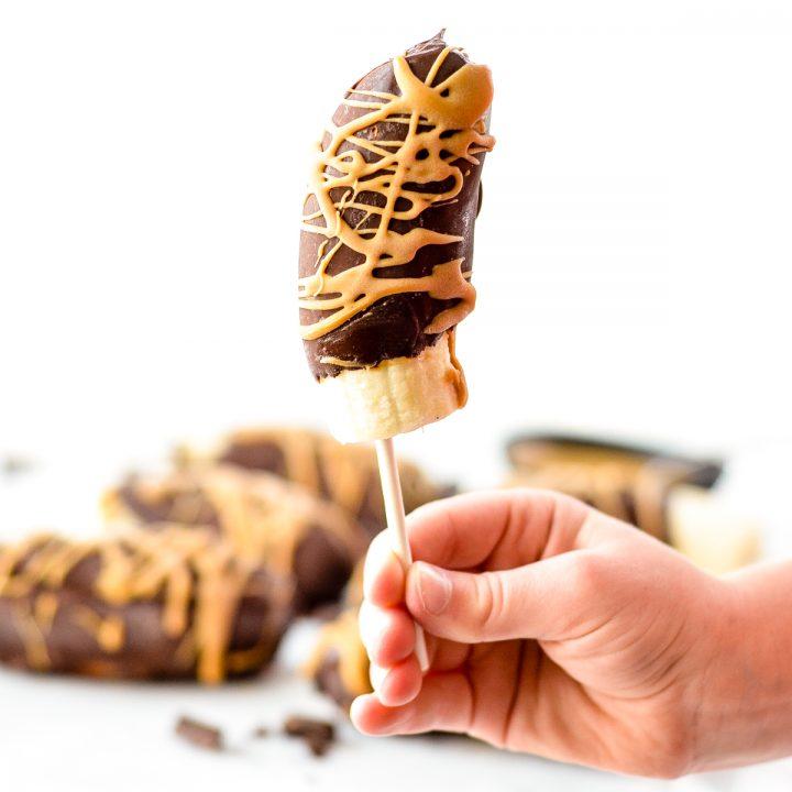 Chocolate covered bananas on a stick with a peanut butter drizzle