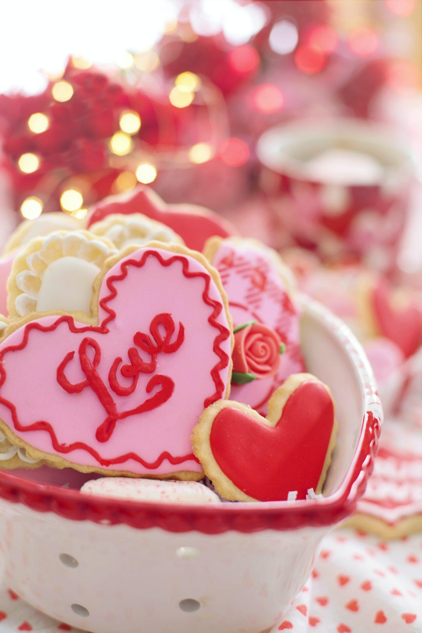 Valentine's heart cookies decorated with pink, red, and white. They are placed in a red and white heart shaped bowl.