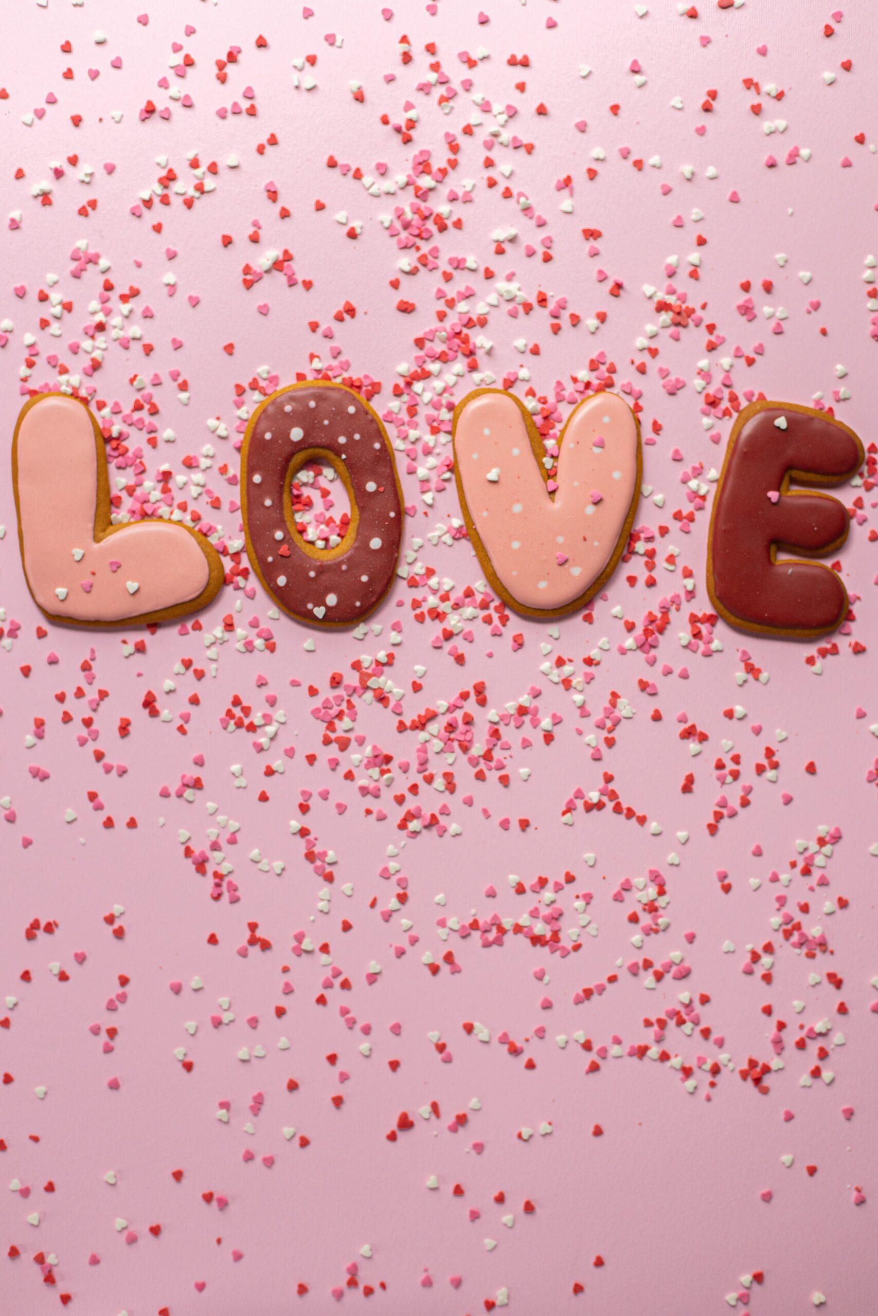 Cookies in letter shape spelling out "Love." They are frosted with pink and maroon frosting and have heart sprinkles.