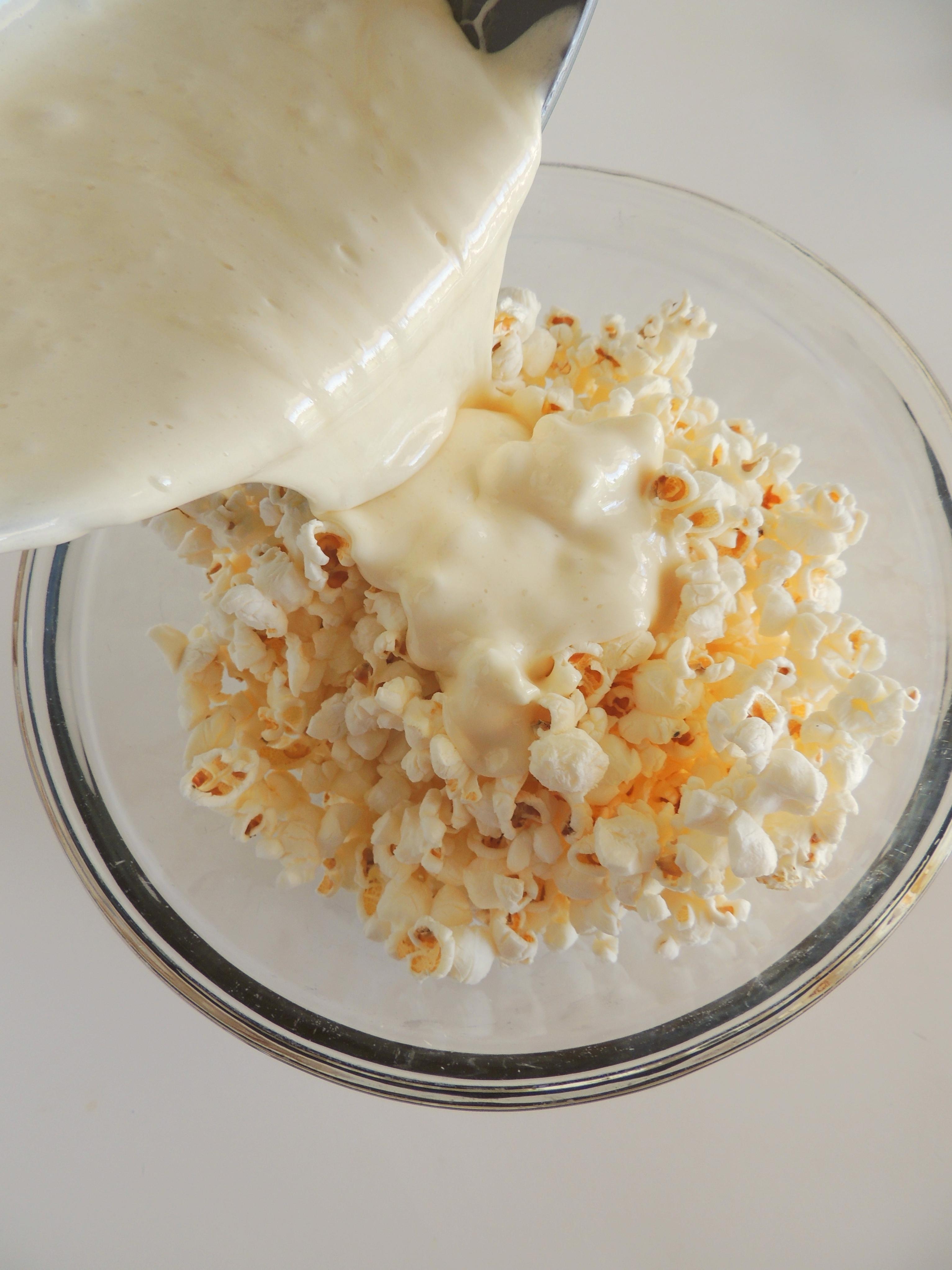 Popcorn in a bowl with marshmallow topping being poured over
