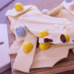 pieces of white chocolate easter bark with cadbury eggs sitting on a wooden cutting board with title above