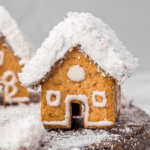 Mini gingerbread house with white forsting on roof, mini door, and mini windows on brown plate with fake snow