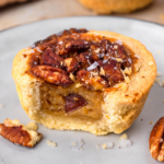 square image of a mini pecan pie with a bite taken out on a grey plate