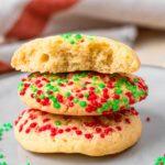 Stack of three Cake Mix Christmas Cookies on a gray plate, decorated with red and green sprinkles. Top cookie is broken to show chewy, tender texture.