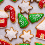 christmas cut out cookies on parchment paper frosted with green, red, and white frosting in the shape of trees, stars, and candy canes.