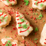 Square image of Christmas Tree Snack Cakes with red frosting and green sprinkles on brown parchment paper