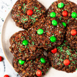 A white plate of no bake chocolate christmas cookies with red and green m&ms from top down view