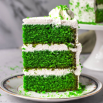 Slice of a three layered green velvet cake with cream cheese frosting on a plate. Side view image to show texture of cake