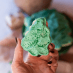 hand holding a christmas tree sugar cookie with green frosting and green sprinkles.