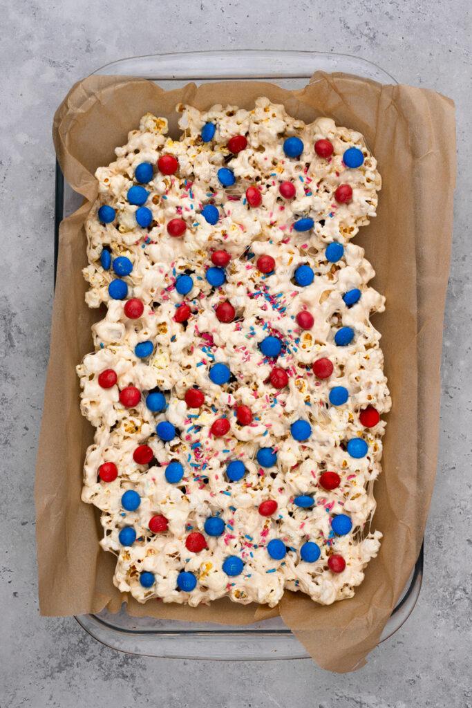 4th of july popcorn with white chocolate and red white and blue sprinkles on brown parchment paper